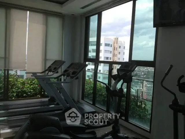 Modern gym with treadmills and large windows offering city views in a high-rise building.