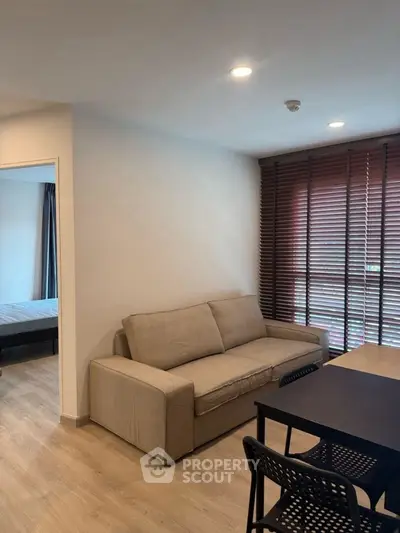 Modern living room with cozy sofa and dining area, featuring wooden blinds and natural light.
