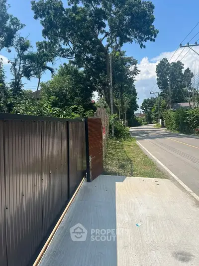 Charming suburban street view with lush greenery and modern gate entrance.