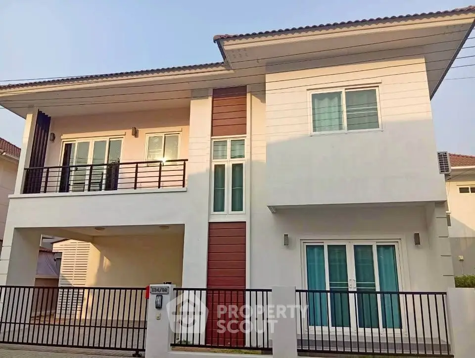 Modern two-story house with balcony and large windows in a suburban neighborhood.
