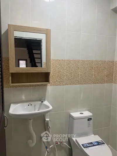 Modern bathroom with sleek sink and toilet, featuring neutral tile design and wooden mirror cabinet.