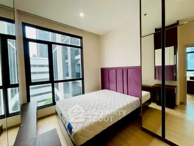 Modern bedroom with large windows and city view, featuring a stylish bed and mirrored wardrobe.