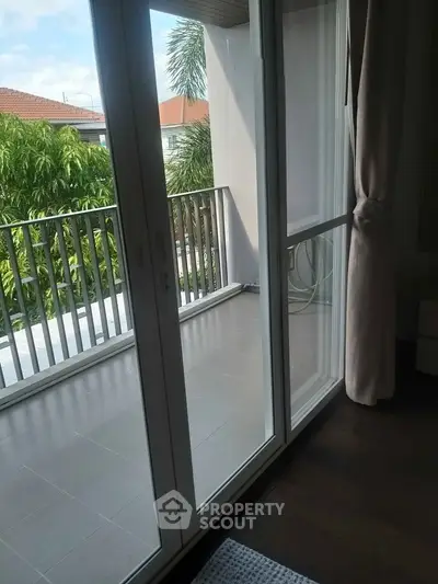 Spacious balcony with sliding glass doors and lush greenery view.