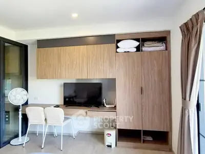 Modern living room with built-in wooden cabinets and TV, featuring a cozy seating area and natural light.