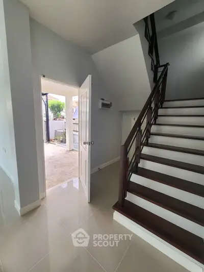 Spacious modern home entrance with elegant staircase and open door to patio.