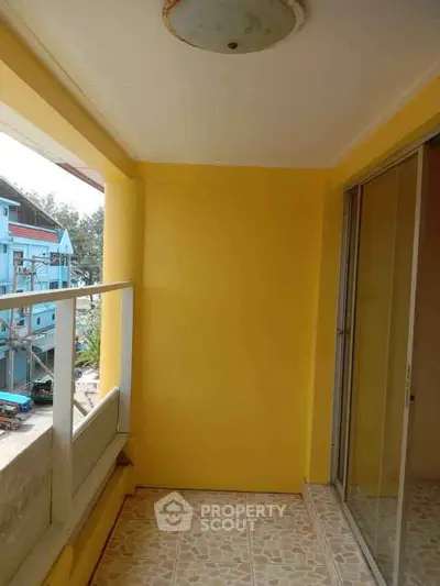 Charming balcony with vibrant yellow walls and sliding glass doors, perfect for relaxation.