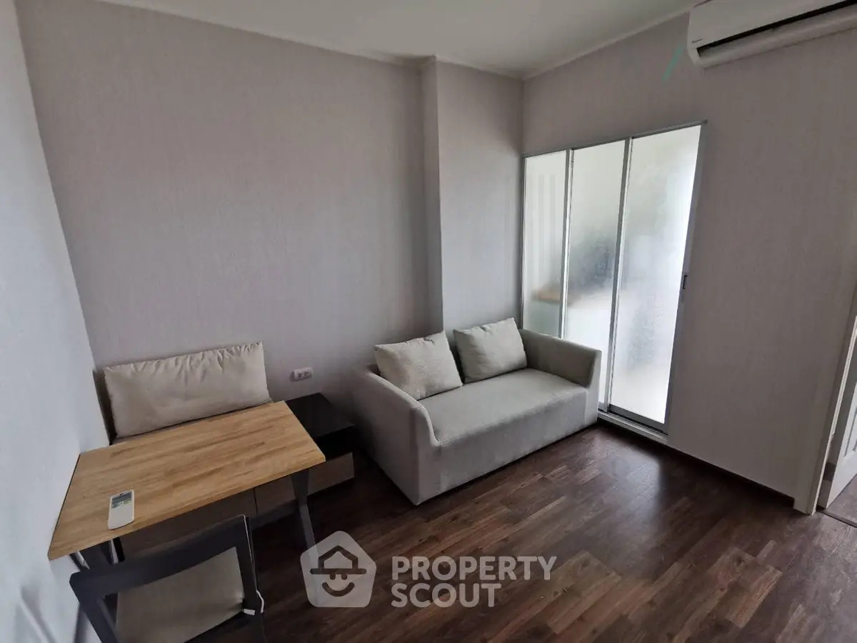 Cozy living room with modern sofa and wooden flooring, featuring a compact dining area and air conditioning.