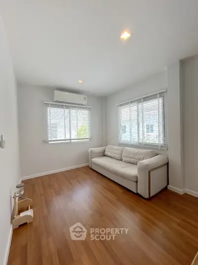Spacious living room with gleaming hardwood floors, ample natural light from large windows, and a modern, comfortable sofa, perfect for relaxing or entertaining guests.