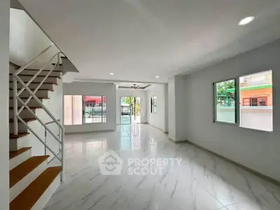 Spacious modern living room with large windows and elegant staircase, perfect for family gatherings.