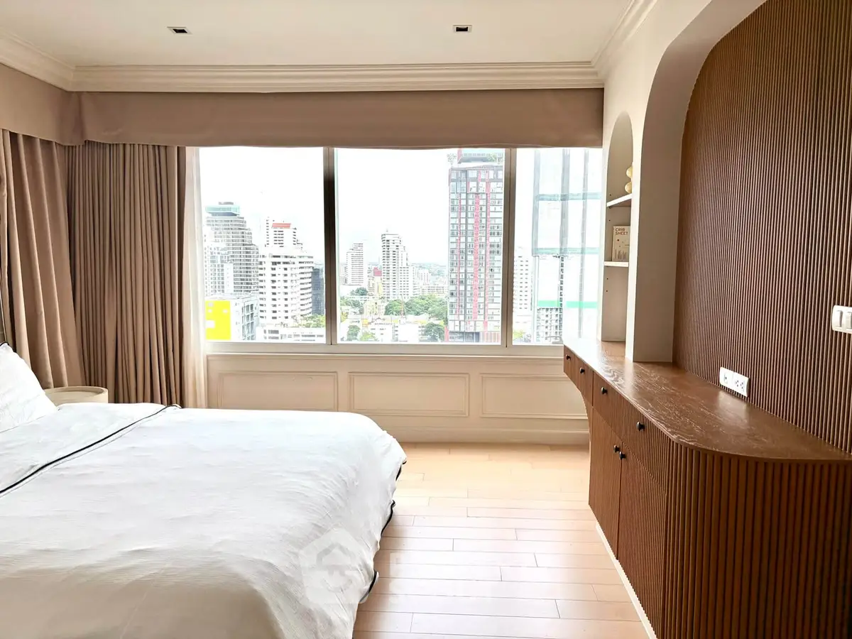 Spacious bedroom with large window offering stunning city views, featuring elegant built-in wooden cabinetry.