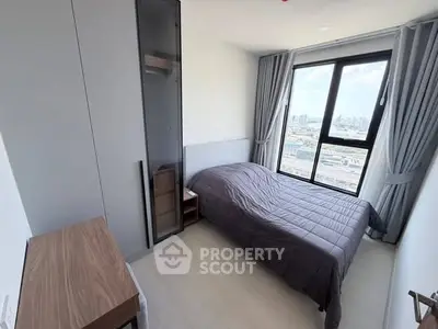 Modern bedroom with city view, featuring sleek furniture and large window for natural light.