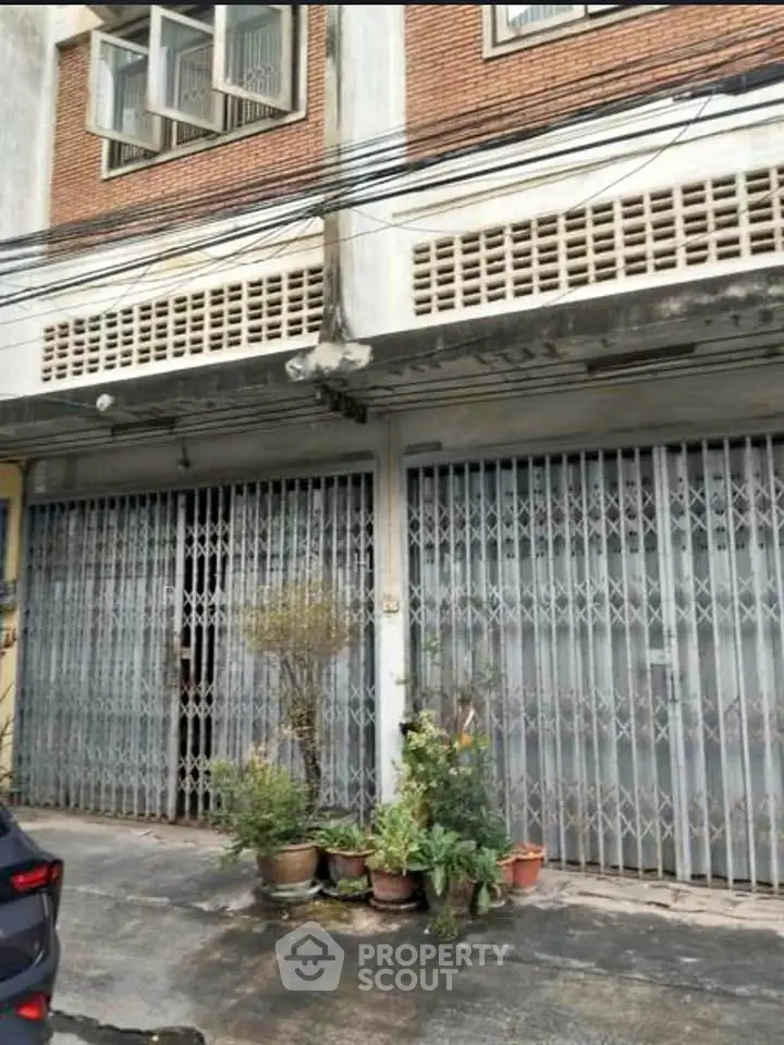 Street view of a commercial building with metal shutters and potted plants.
