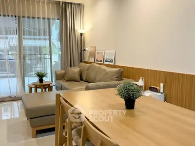 Modern living room with cozy seating and stylish decor, featuring a large window with balcony view.