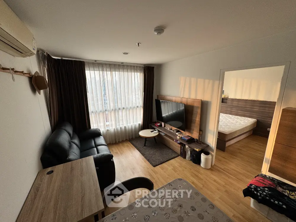 Cozy living room with modern furniture and natural light, adjacent to a bedroom with a comfortable bed.