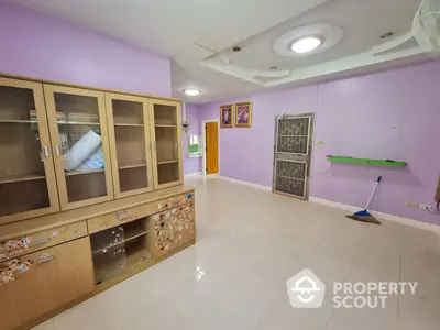 Spacious living room with large wooden cabinets and bright lilac walls, featuring modern lighting and pristine tiled flooring.