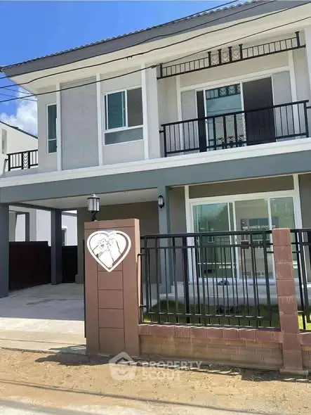 Modern two-story house with balcony and gated entrance in sunny neighborhood.