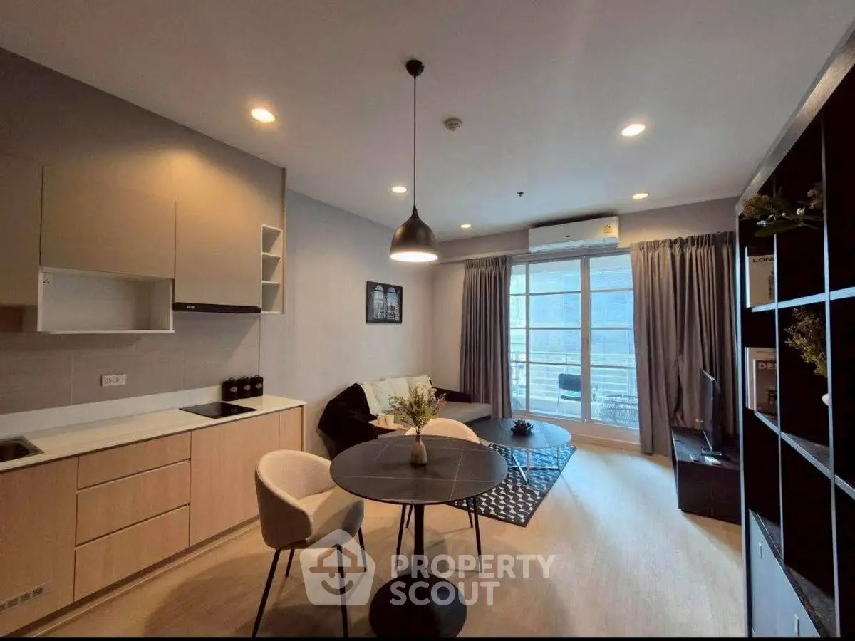 Modern living room with open kitchen, stylish decor, and large windows offering natural light.