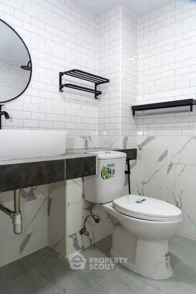 Modern bathroom with white subway tiles and marble accents, featuring a sleek round mirror and contemporary fixtures.