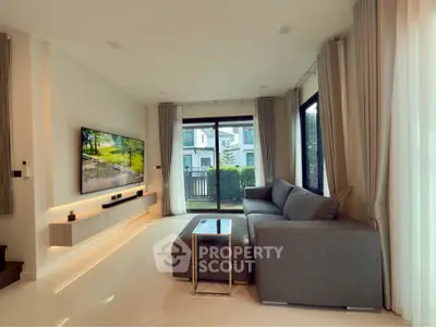 Modern living room with large sofa and wall-mounted TV, featuring elegant decor and natural light.