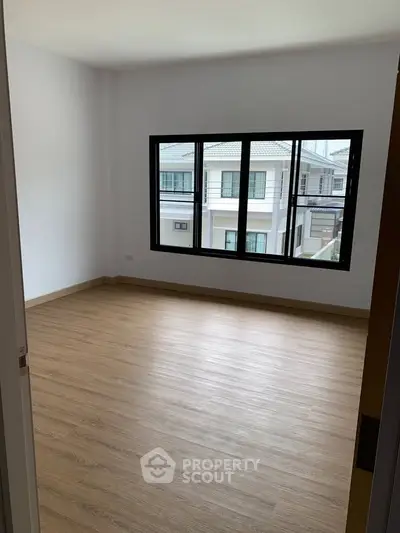 Spacious empty room with wooden flooring and large window view