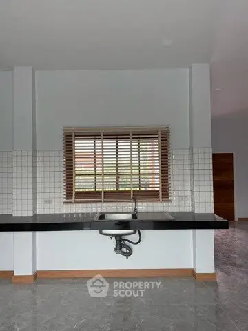 Modern kitchen with sleek countertop and window blinds, featuring a minimalist design and tiled backsplash.