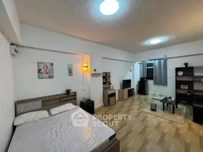 Spacious studio apartment with modern decor and wooden flooring, featuring a cozy bed and stylish living area.