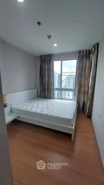 Spacious bedroom with large window offering city views, featuring a comfortable bed and elegant curtains.