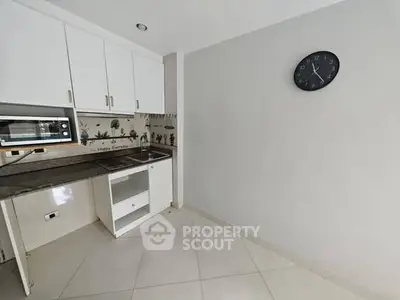 Compact kitchen with white cabinets and wall clock, ideal for small apartments.
