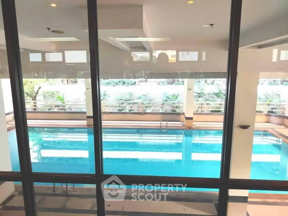 Luxurious indoor swimming pool with glass walls and lush greenery view, perfect for relaxation and leisure.