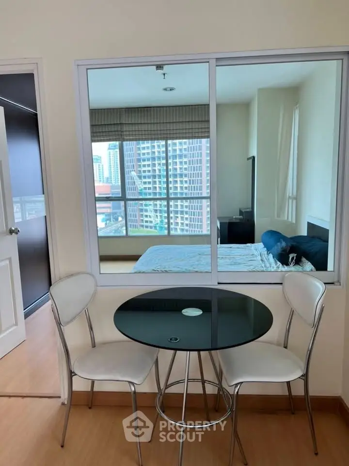 Modern apartment with glass partition and city view, featuring a cozy dining area and stylish bedroom.