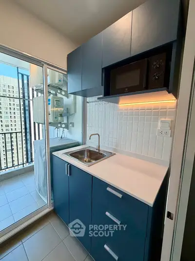 Modern compact kitchen with blue cabinets and balcony view in high-rise apartment