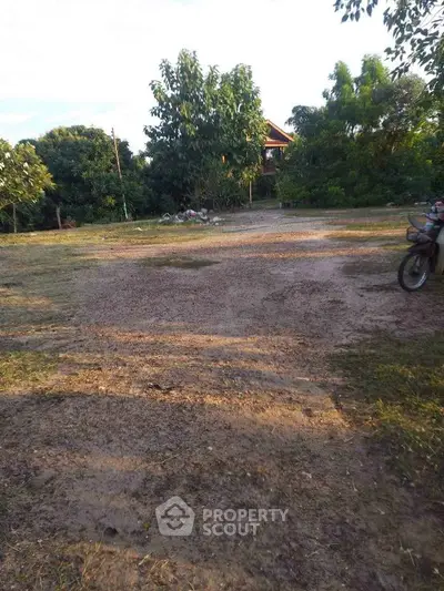 Spacious rural land with lush greenery and a distant house, ideal for development or agriculture.