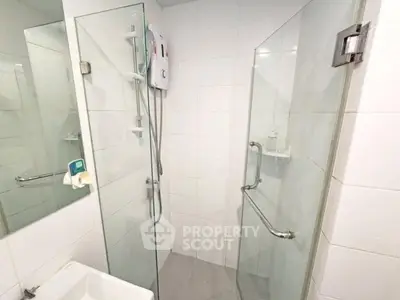 Modern bathroom with glass shower enclosure and sleek white tiles.