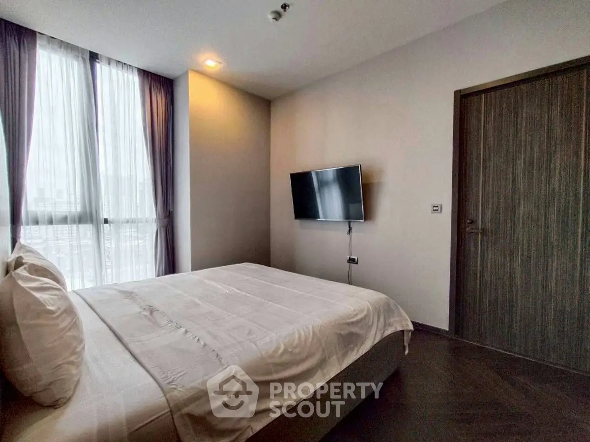 Modern bedroom with large window and wall-mounted TV in a stylish apartment.