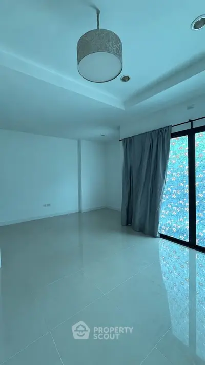 Spacious empty room with large window and modern light fixture, ideal for customization.