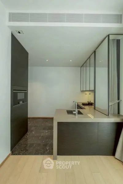 Modern kitchen with sleek design and open layout, featuring dark cabinetry and light wood flooring.