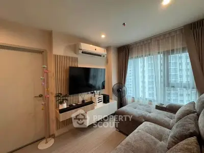 Modern living room with cozy sectional sofa, wall-mounted TV, and large window with city view.