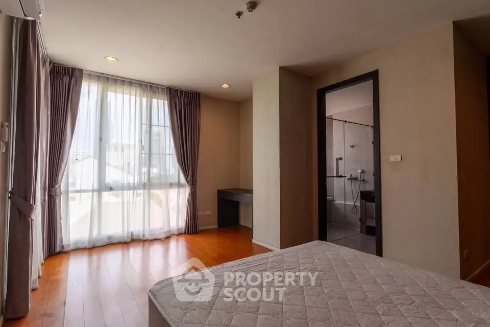 Spacious bedroom with large window and wooden flooring in modern apartment