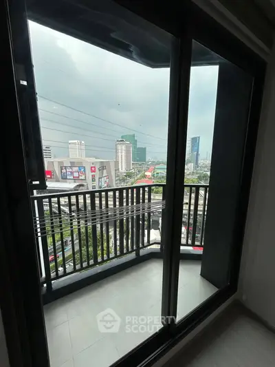 Modern city view from a high-rise apartment balcony with glass doors.