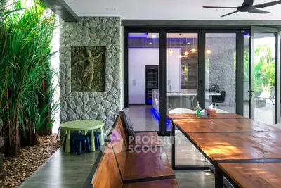 Modern open-plan living area with stone wall, wooden dining table, and lush greenery for a serene ambiance.