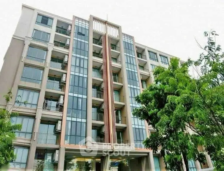 Modern apartment building with glass facade and lush greenery.