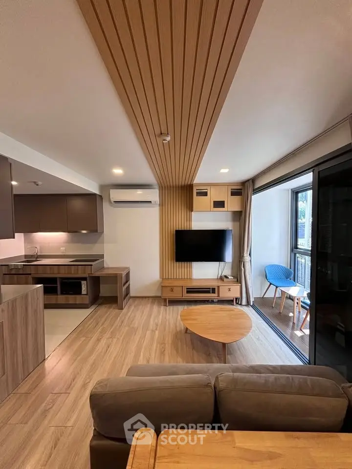 Modern living room with open kitchen, wooden accents, and balcony access in a stylish apartment.