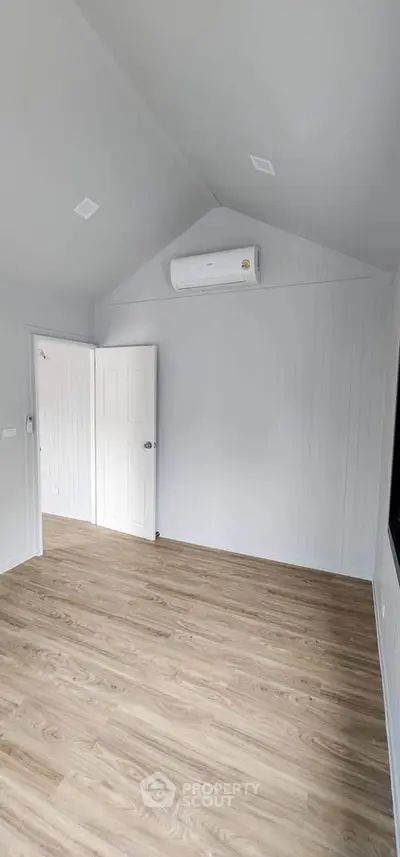 Spacious empty room with wooden flooring and air conditioning, perfect for customization.