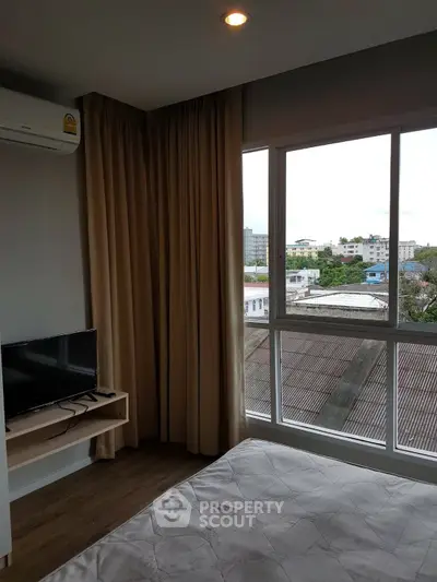 Cozy bedroom with large window offering city view, featuring a mounted TV and air conditioning.