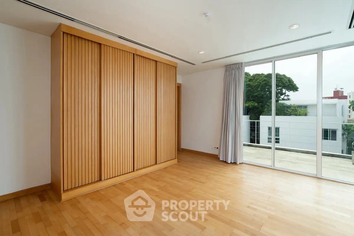 Spacious room with wooden flooring and large sliding doors opening to a balcony with a view.