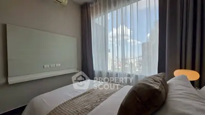 Modern bedroom with city view and natural light through large window.