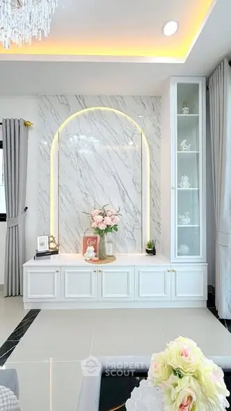 Elegant living room with marble accent wall and built-in shelving, featuring soft lighting and floral decor.