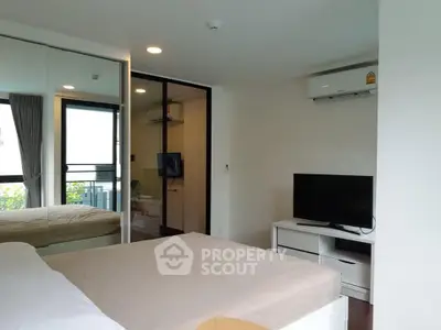 Modern bedroom with mirrored closet and balcony view, featuring sleek furniture and air conditioning.