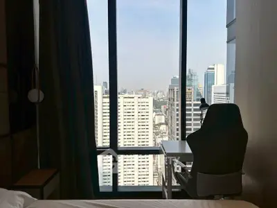 Modern bedroom with city view, featuring a sleek desk and chair by the window.