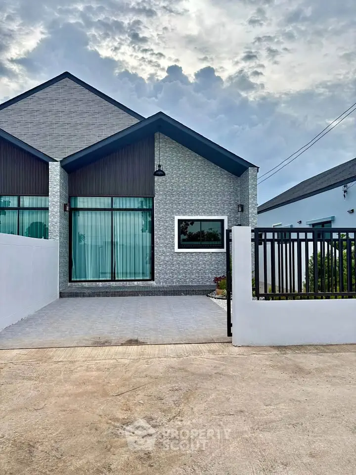 Modern single-story house with sleek design and spacious driveway under a cloudy sky.